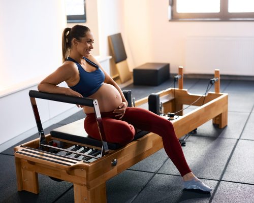 Happy pregnant woman taking a break while working out at Pilates studio. Copy space.