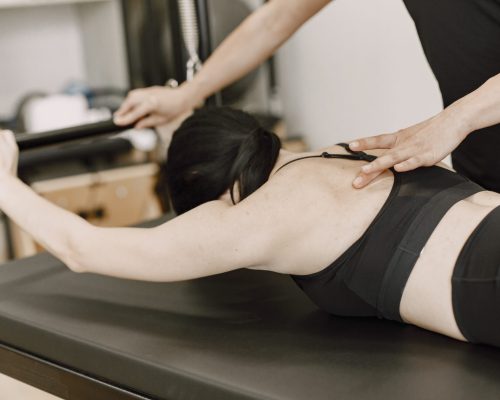 Young fit woman with a female trainer in gym. Woman wearing black sportwear. Caucasian girl lying on her belly.